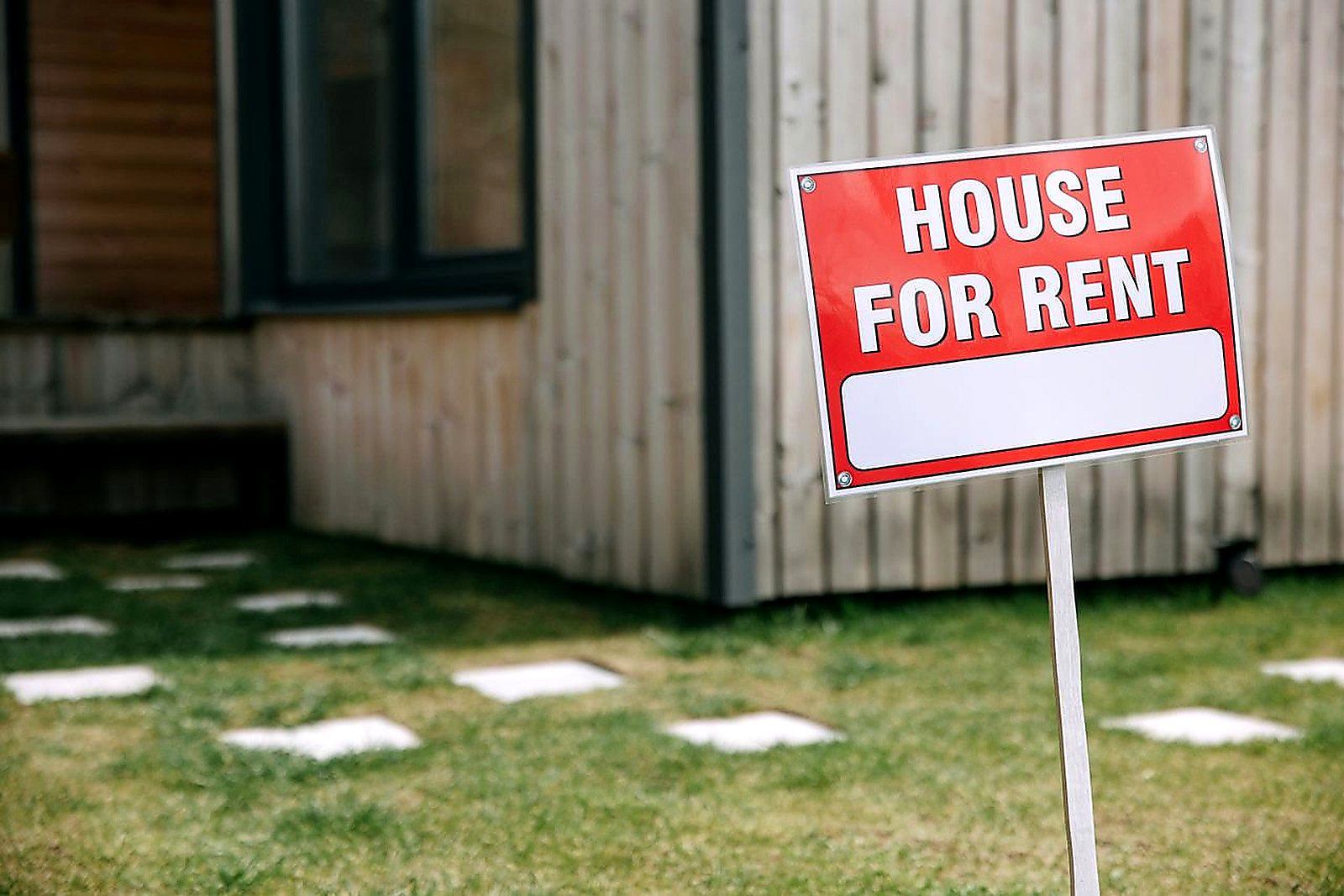 Free A modern wooden house with a prominent 'House for Rent' sign in the green yard. Stock Photo